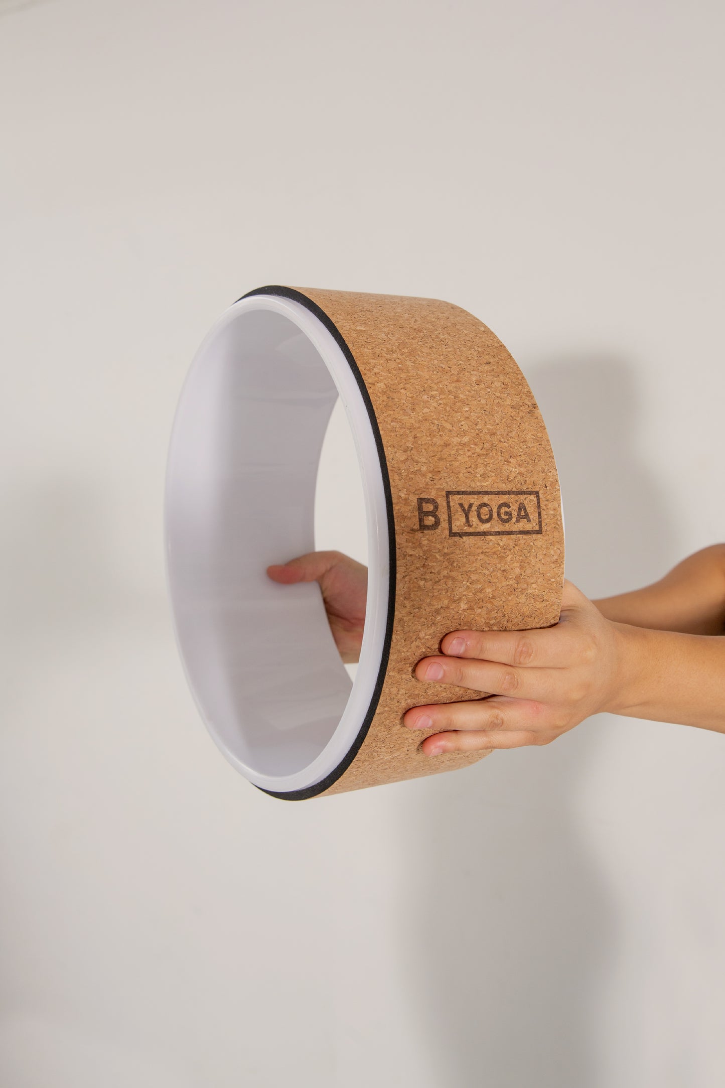 The Freedom Wheel - a cork yoga wheel by BYOGA will help you open your heart, chest and shoulders while freeing up your upper back. Photographed on a white background with someones hands holding the yoga wheel outstretched..