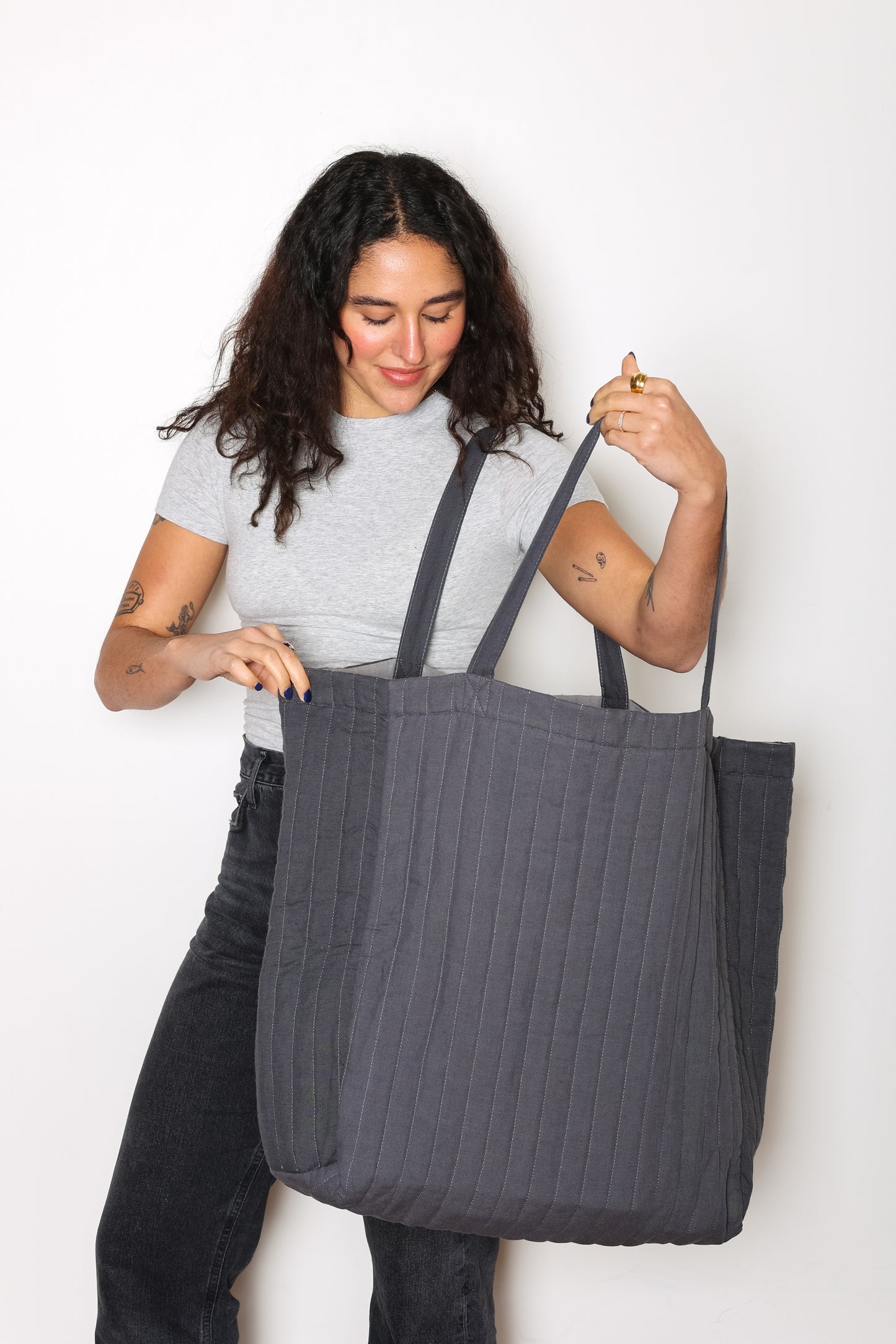 Smiling Model opening up Charcoal ESME oversized quilted tote - photographed on a white background