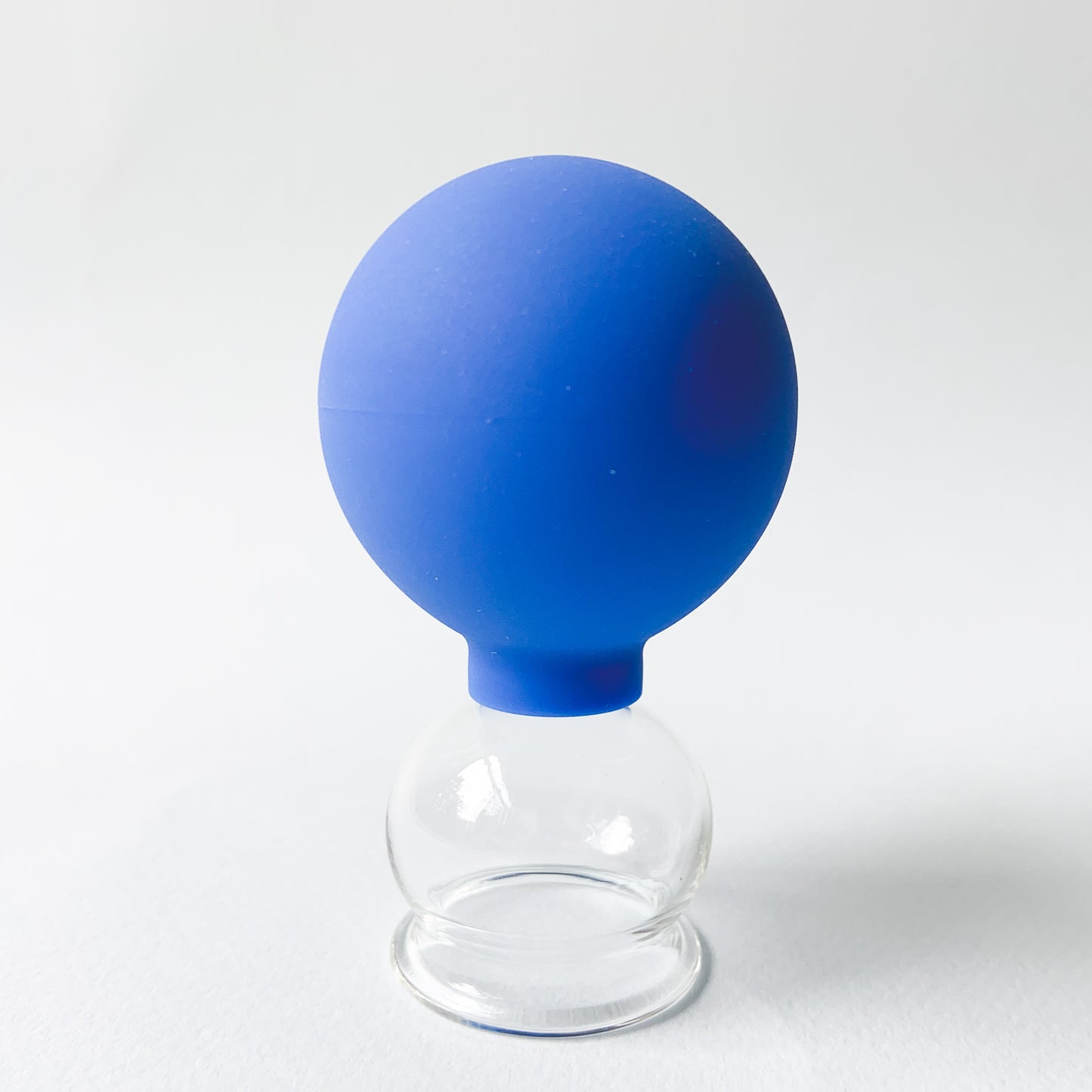 Single Glass Facial Cup with a blue rubber ball - photographed on a light grey background.