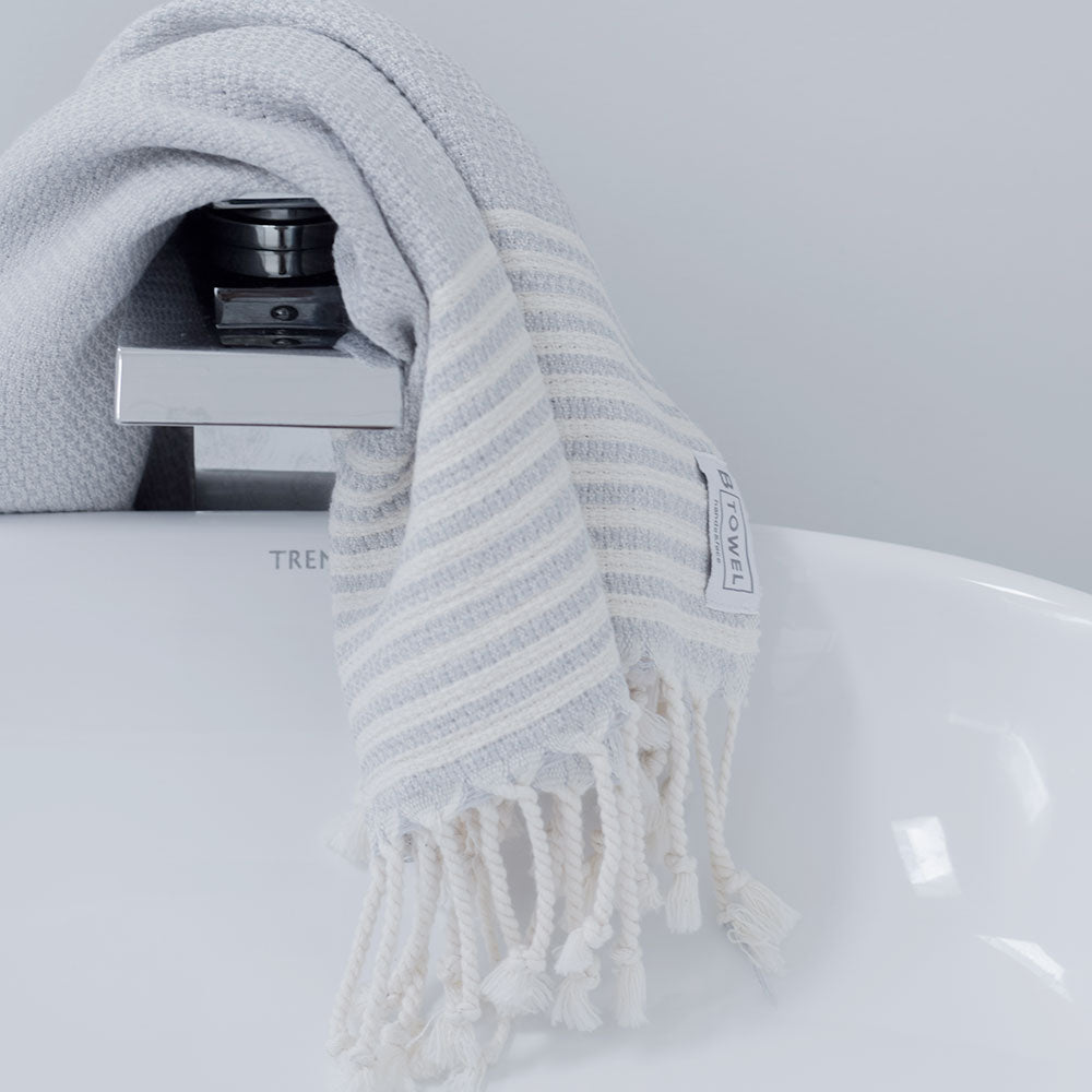 Lifestyle shot - Stone Grey - hand and face towel by B Yoga - Turkish Cotton laying on the tap of a white sink