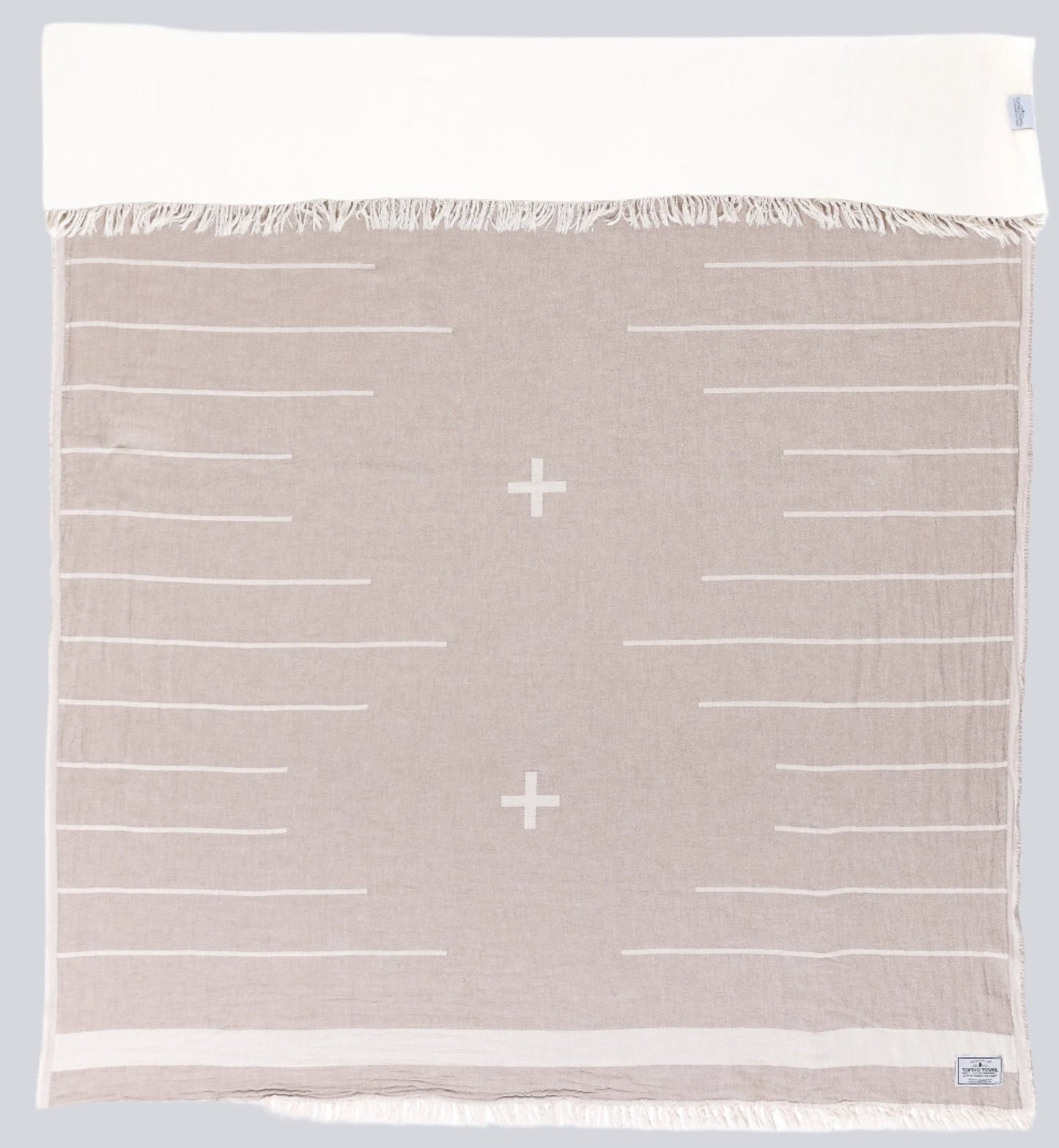 Beige throw with white lines and two a white fringe edge - Tofino Towel Company label on the bottom Right corner