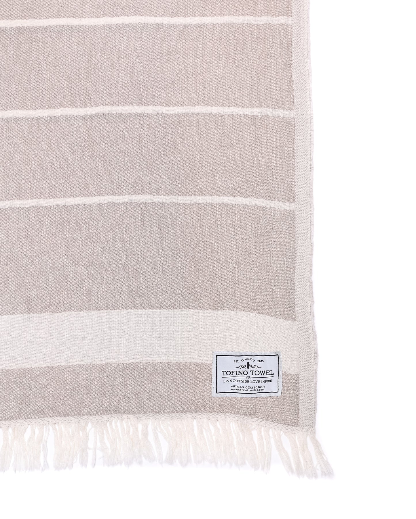 Close up of Beige throw with white lines and two a white fringe edge - Tofino Towel Company label on the bottom Right corner