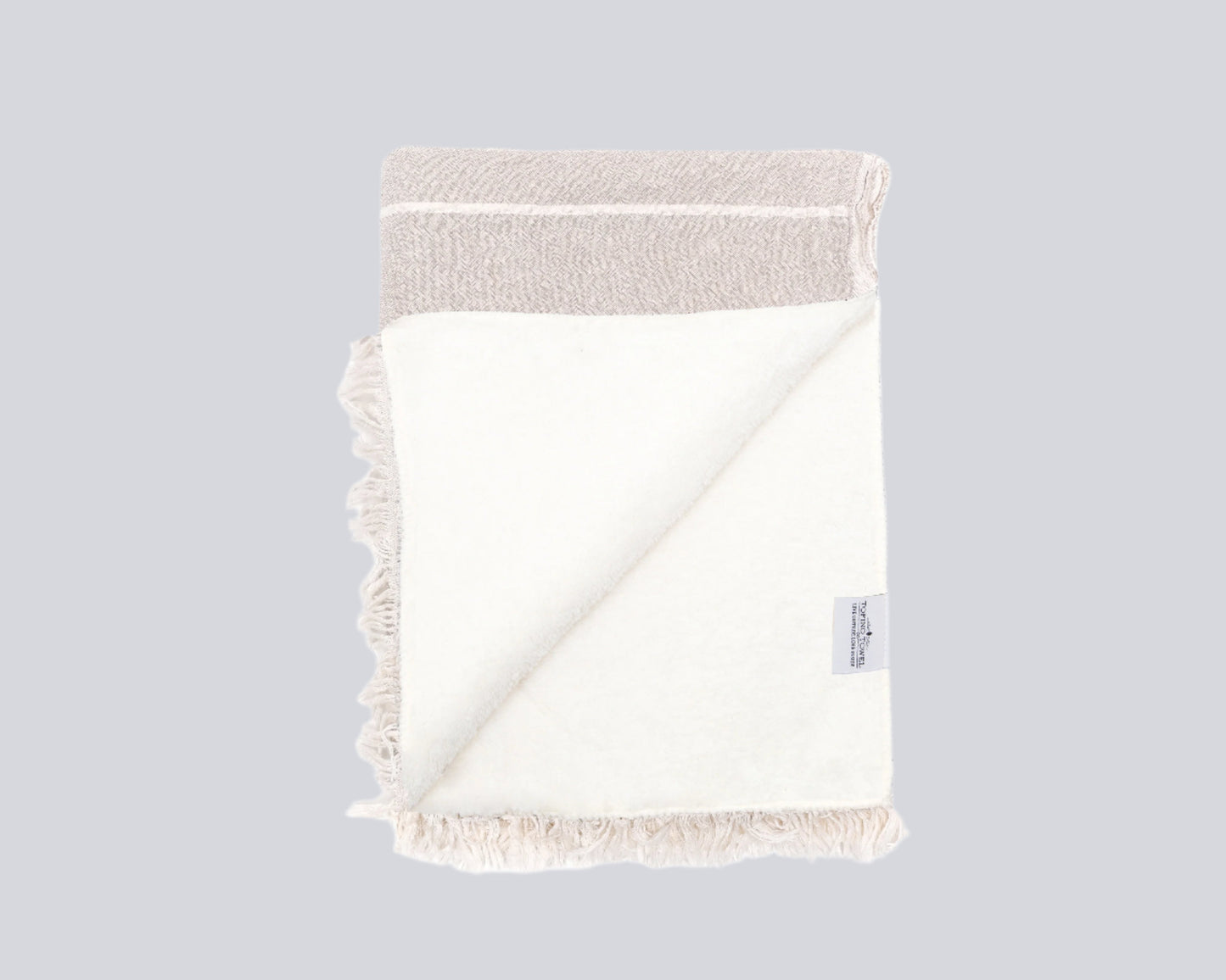 Open pannel of fleece lining on the inside of the Beige throw with white lines and two a white fringe edge - Tofino Towel Company label on the bottom Right corner