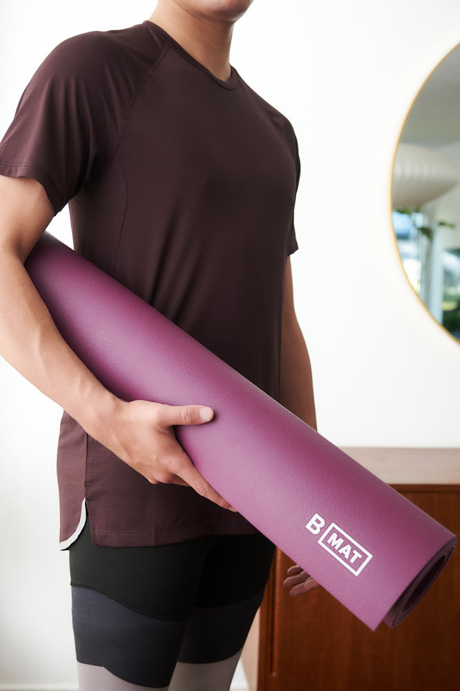 
                  
                    B Yoga - Strong 6mm yoga mat in beetroot, being carried by a fit man
                  
                