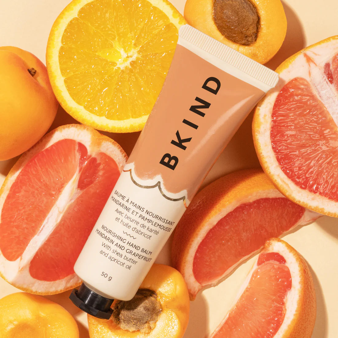 BKIND - Nourishing Hand Balm - Mandarin and Grapefruit - displayed with fresh cut citrus as a background - the tube of BIND hand balm is well lit and bright with vertical writing of BKIND.