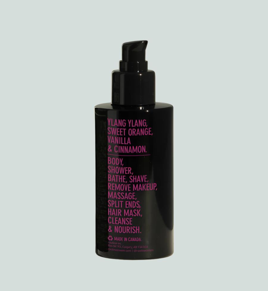 Back shot of the product, large magenta writing on a black bottle with black pump. Ingredients are listed in large format, Ylang ylang, Sweet Orange, Vanilla & Cinnamon.