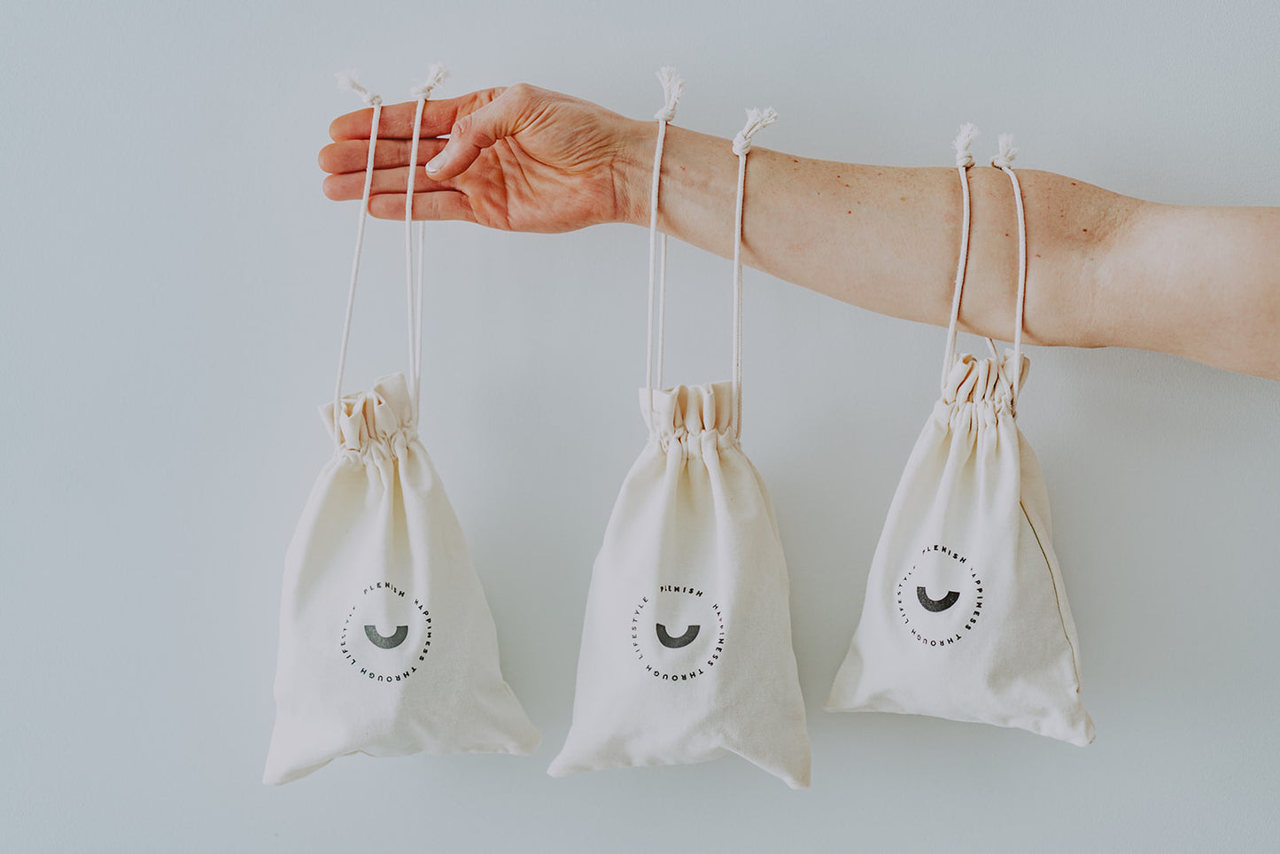 Three Large Drawstring Canvas - Plenish Brand Travel Bag displayed on an outstretched arm