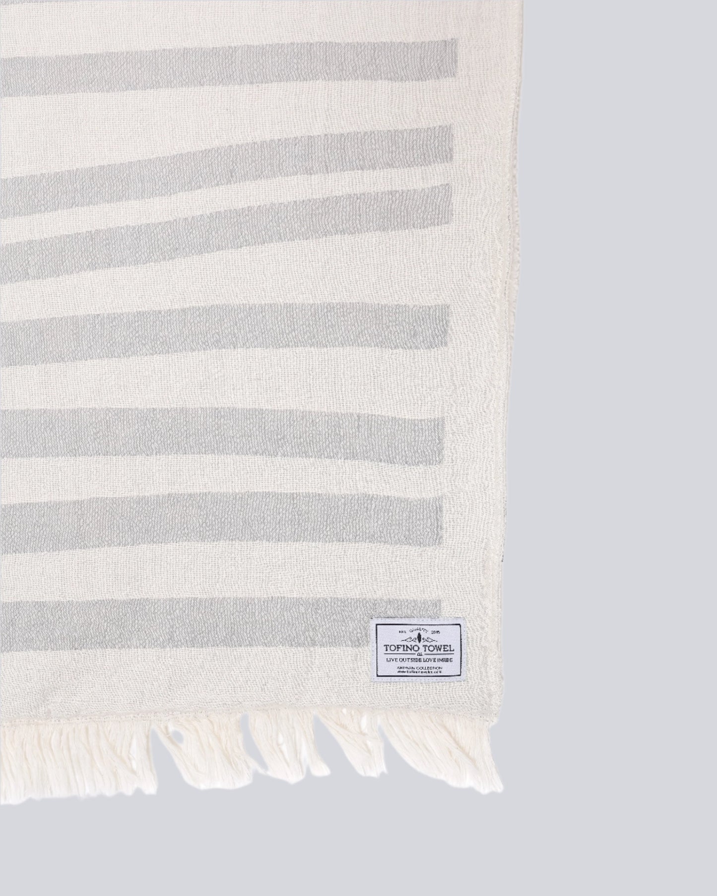 Close up of - The Rowan Throw from the Tofino Towel Company - In Pewter colour with horizontal ligth grey lines on a white blanket - Turkish Cotton on one side and fleece lined on the other.