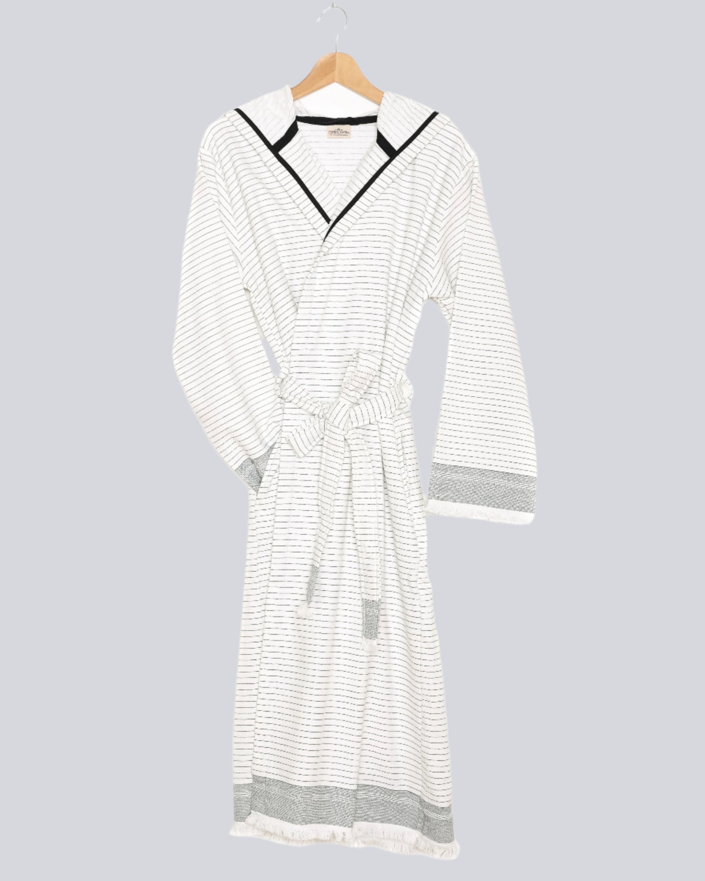 The Silas Robe from Tofino Towel Company - off white with black thin horizontal stripes and a hood.  Photographed on a wooden hanger on a white background.