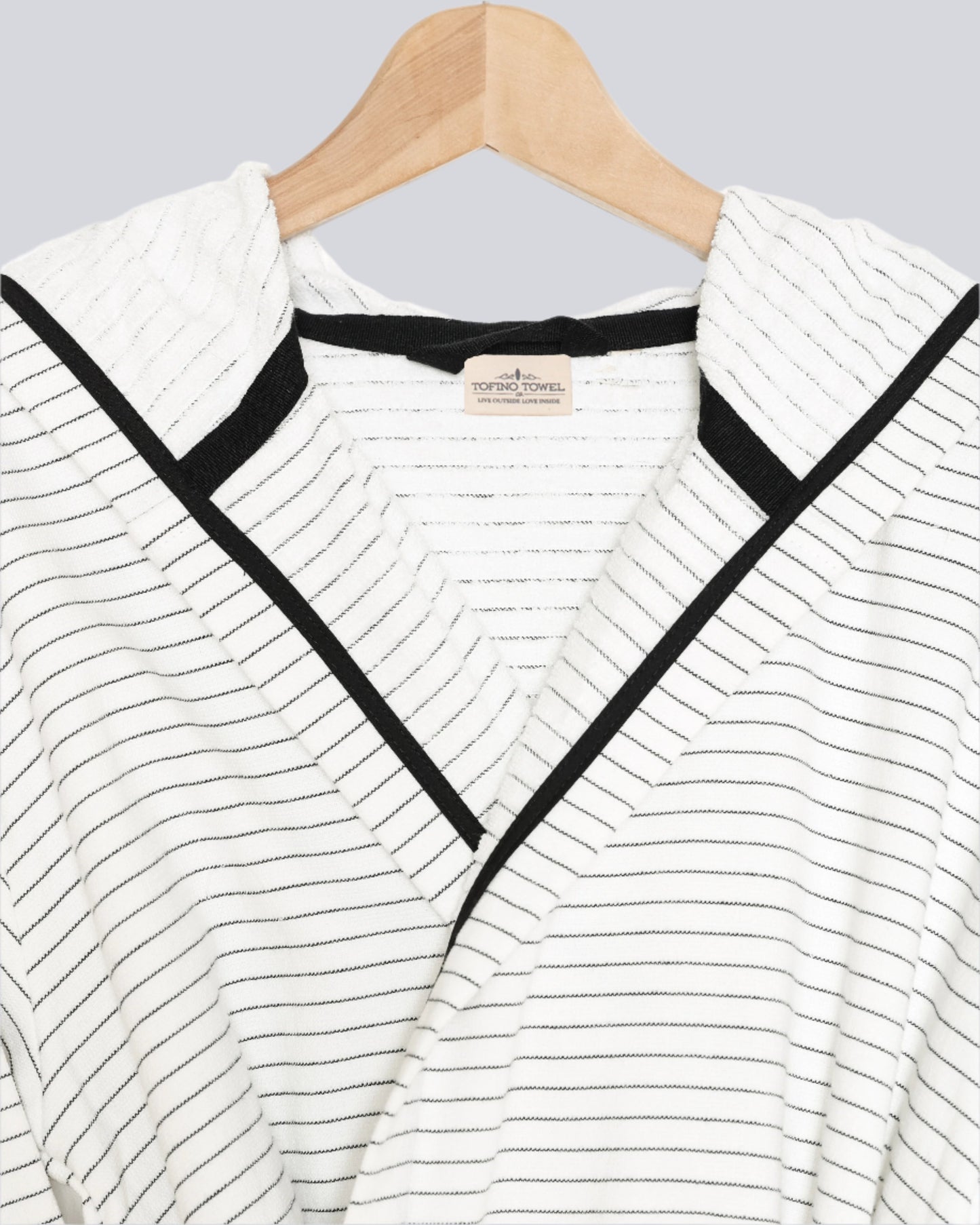 Close up of The Silas Robe from Tofino Towel Company - off white with black thin horizontal stripes and a hood.  Photographed on a wooden hanger on a white background.