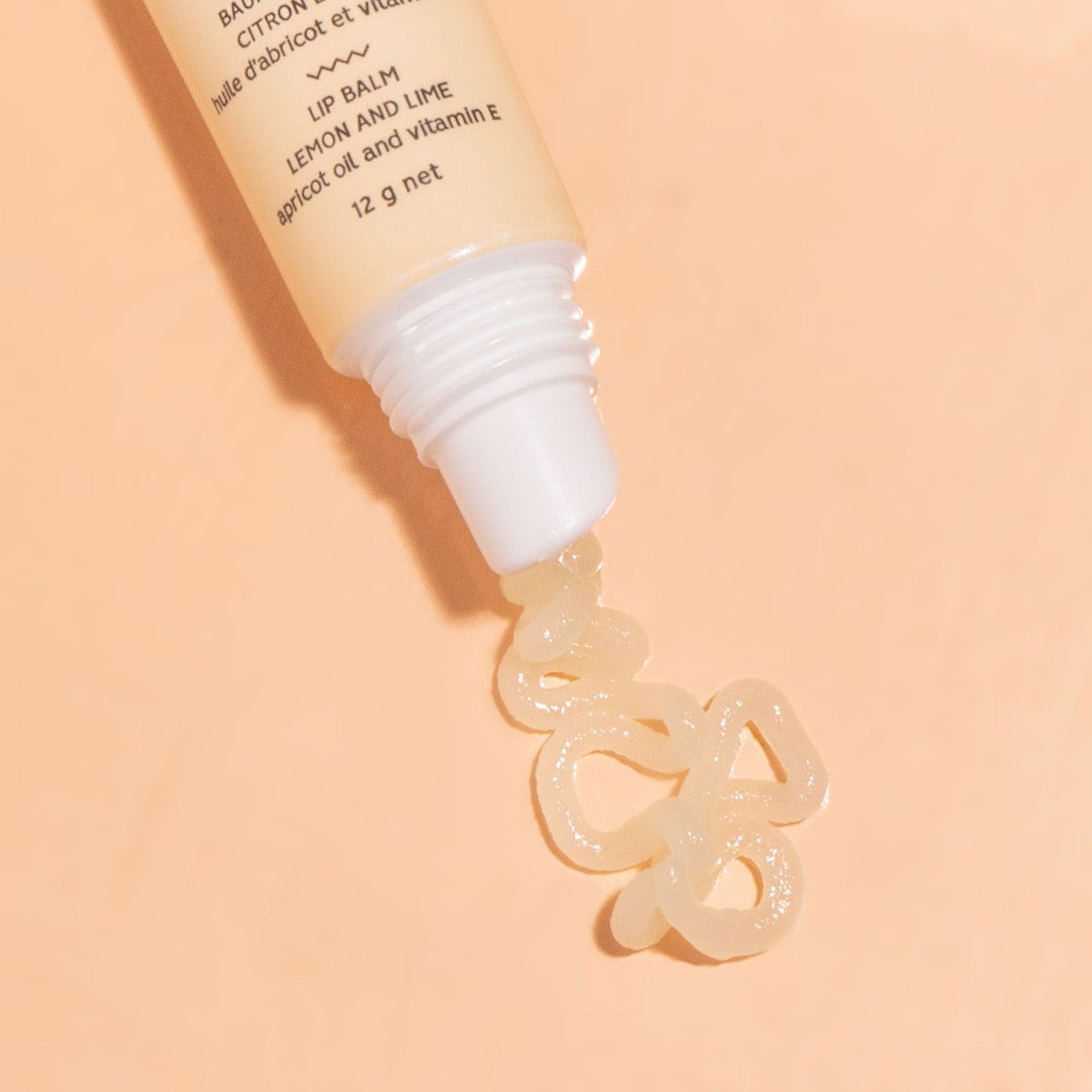 Close up picture of BKIND - Lemon and Lime lip balm displayed on a peach background showing lip gloss squeezed out of the tube onto the background - close up shot.