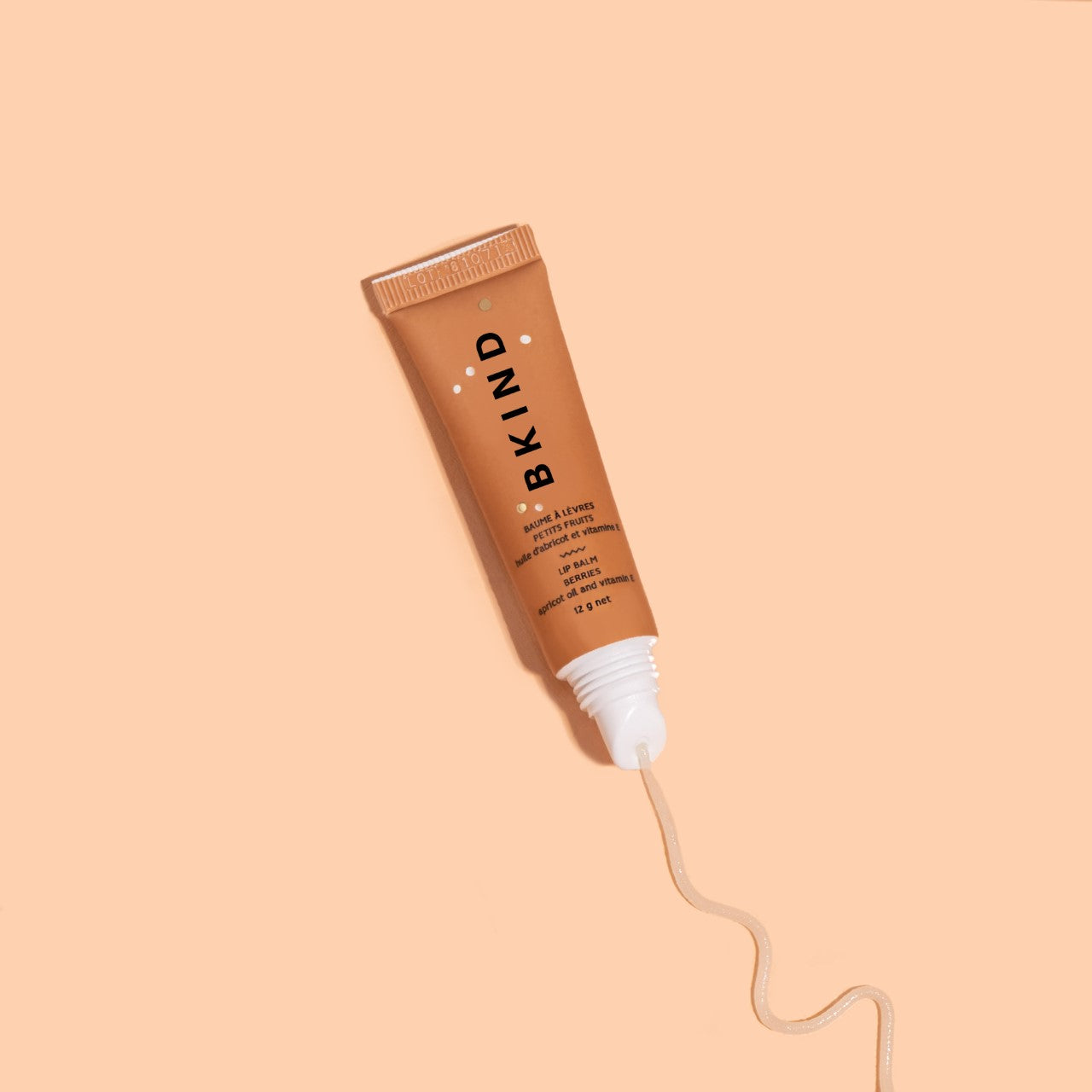 BKIND lip balm - berries - displayed with a smooth gloss of the product squeezed out onto the peach background.  The tube of orange/brown gloss is well lit with BKIND written vertically.
