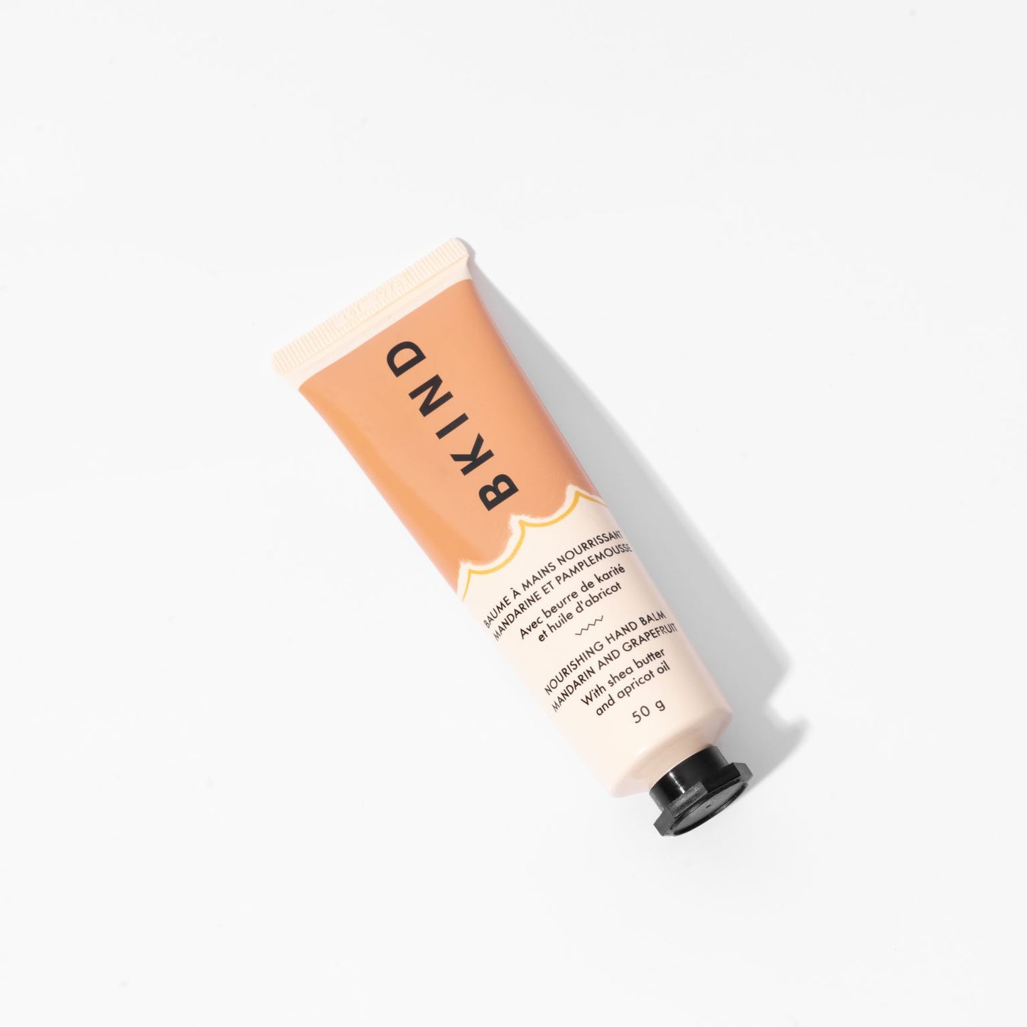 BKIND - Nourishing hand balm - Mandarin and Grapefruit is displayed on a white background with the orange/brown tube lying down with vertical writing of BKIND on the label.