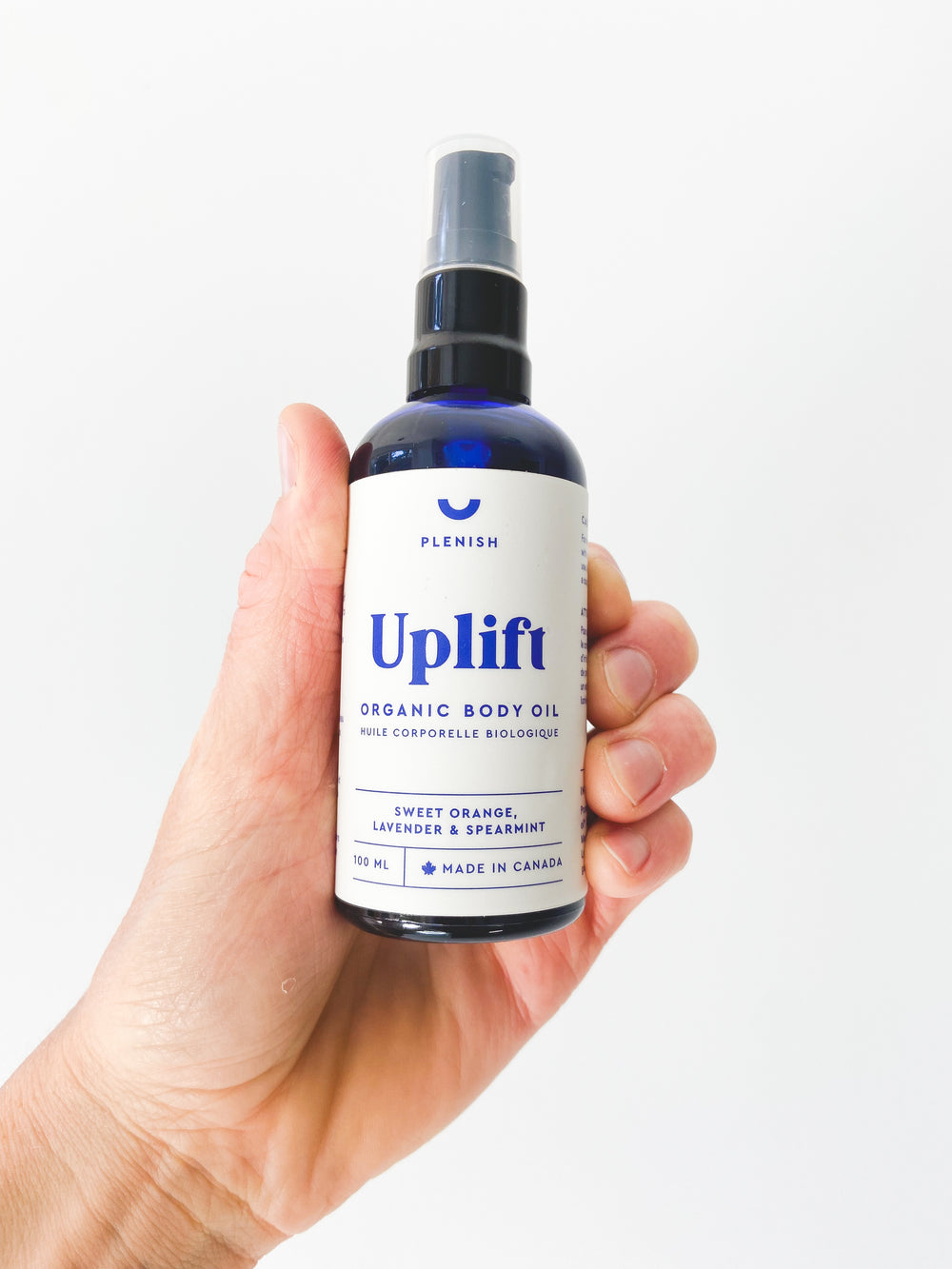 A photos of UPLIFT - Organic body oil, held in a hand - made in Canada 100mL of Sweet Orange, Lavender and Spearmint essential oils.