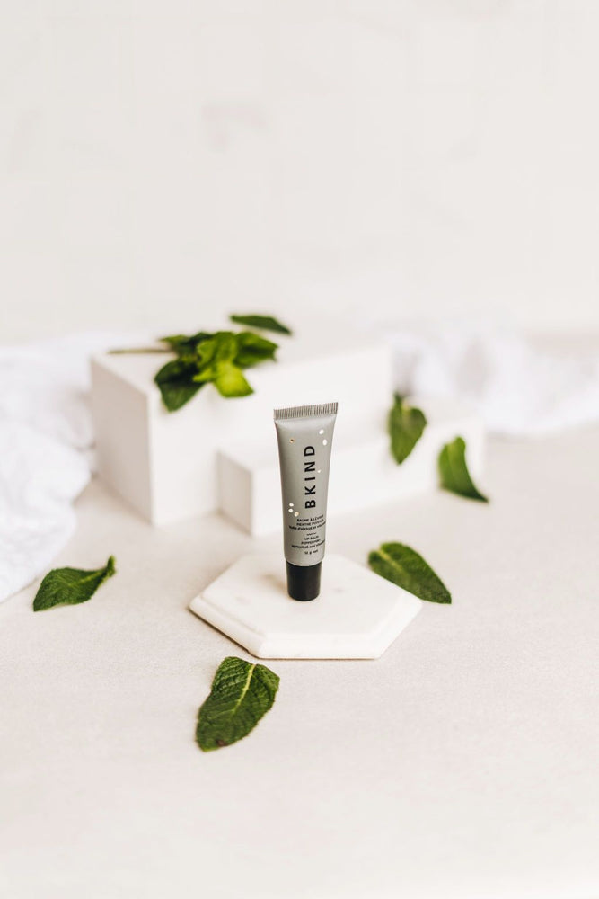 
                  
                    BKIND natural vegan lip balm - Peppermint - Displayed with cut peppermint leaves on three white display blocks - small grey tube of BKIND lip balm with a black lid standing upright on the white blocks.
                  
                