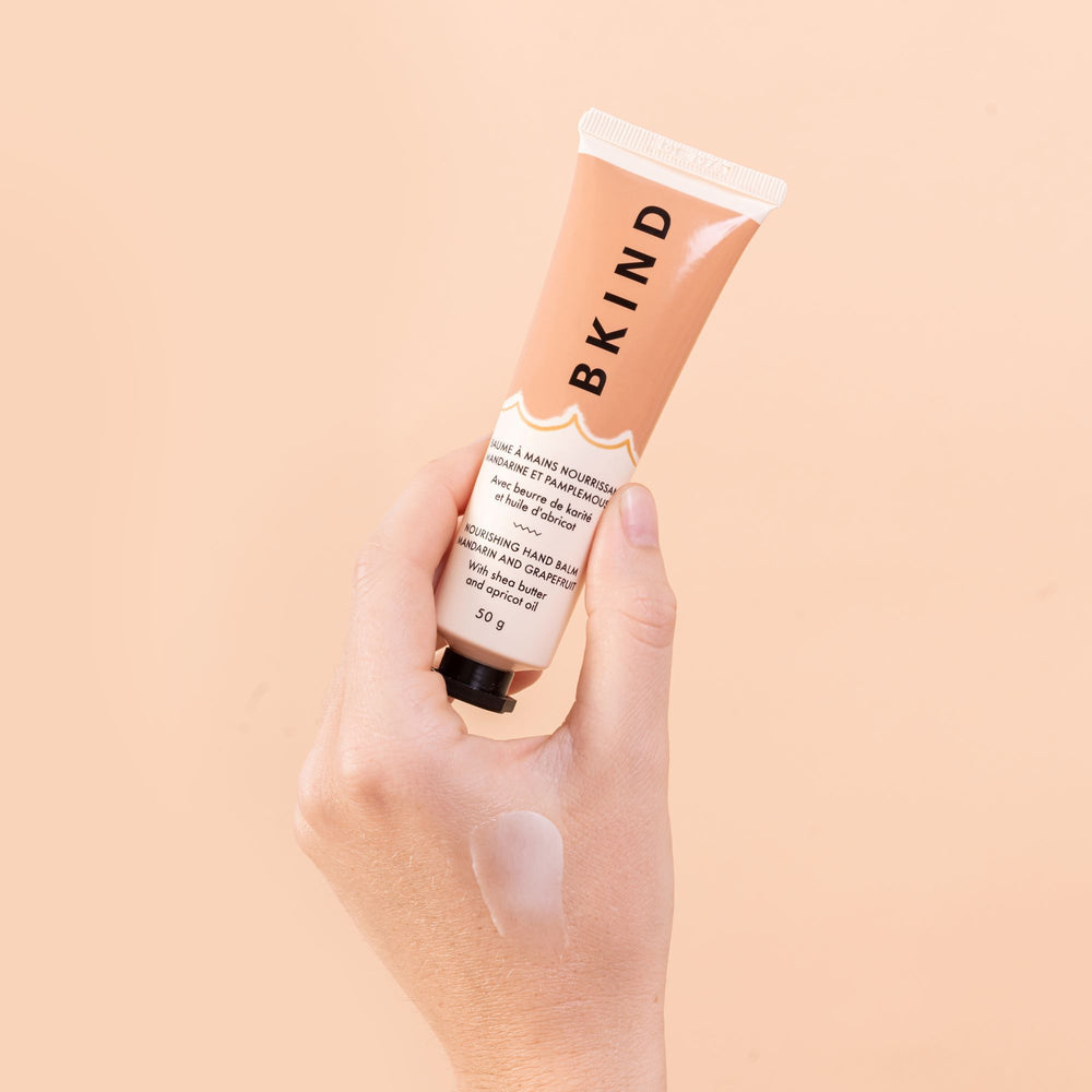 
                  
                    BKIND - Nourishing hand balm - Mandarin and Grapefruit - this tube is held by someones hand and shown close up - well lit on a light peach background with vertical writing of BKIND on the product label.
                  
                